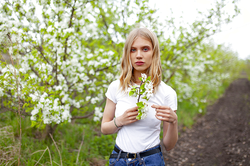 Portrait of woman holding branch of apple tree in orchard