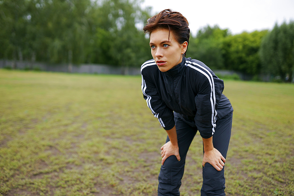 Portrait of young woman standing with hands on knees during sports training