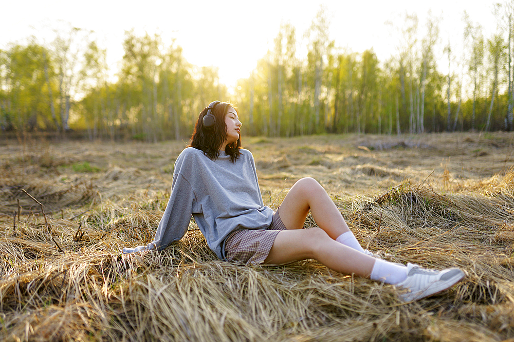 Brunette woman sitting in meadow and listening to music 