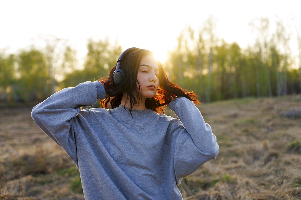 Portrait of woman listening to music with closed eyes in meadow at sunset