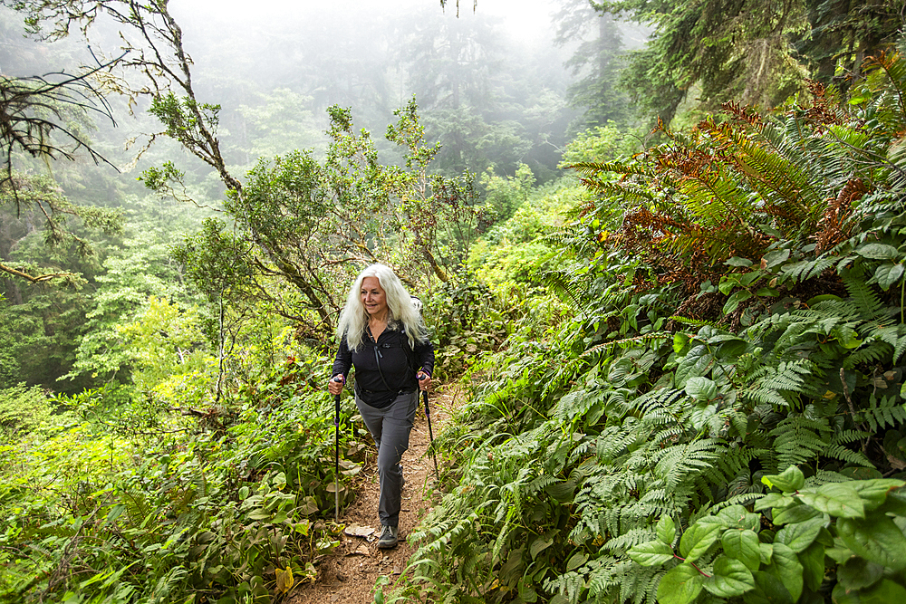 Senior woman hiking on hill with nordic walking poles