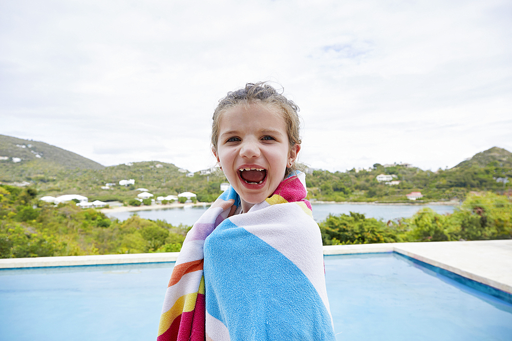 Portrait of smiling girl (6-7) wrapped in towel by swimming pool