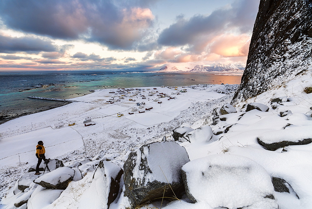 Photographer on the snow admires the fishing village under a colorful sky Eggum, Vestvagoy (Vest-Vagoy) Island, Lofoten Islands, Arctic, Norway, Scandinavia, Europe