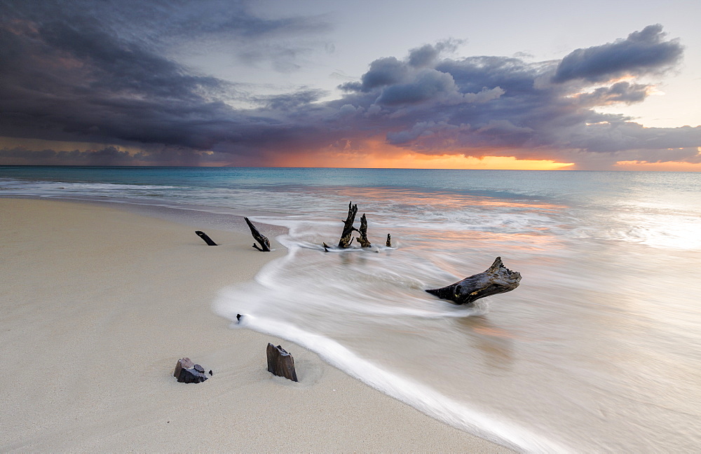 Caribbean sunset frames tree trunks on Ffryes Beach, Antigua, Antigua and Barbuda, Leeward Islands, West Indies, Caribbean, Central America