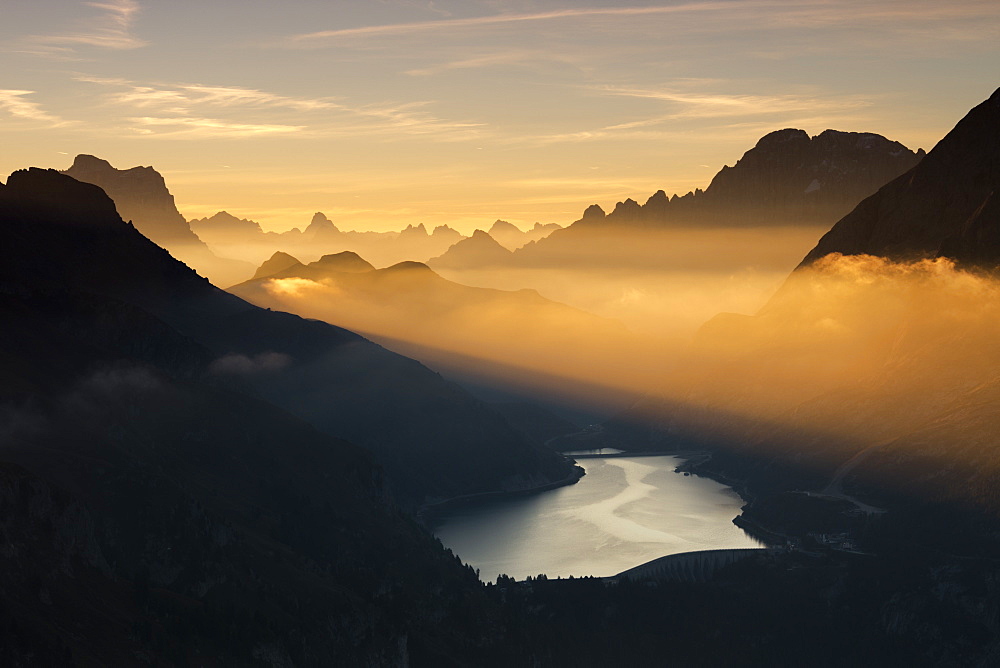 Orange light beam and mist on peaks of Dolomiti and Fedaia Pass, Cima Belvedere, Val di Fassa, Trentino-Alto Adige, Italy, Europe