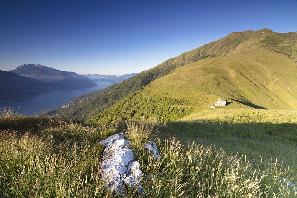 Sunbeam on Church of San Bernardo lights up the landscape around the blue water of Lake Como at dawn, Musso, Lombardy, Italy, Europe