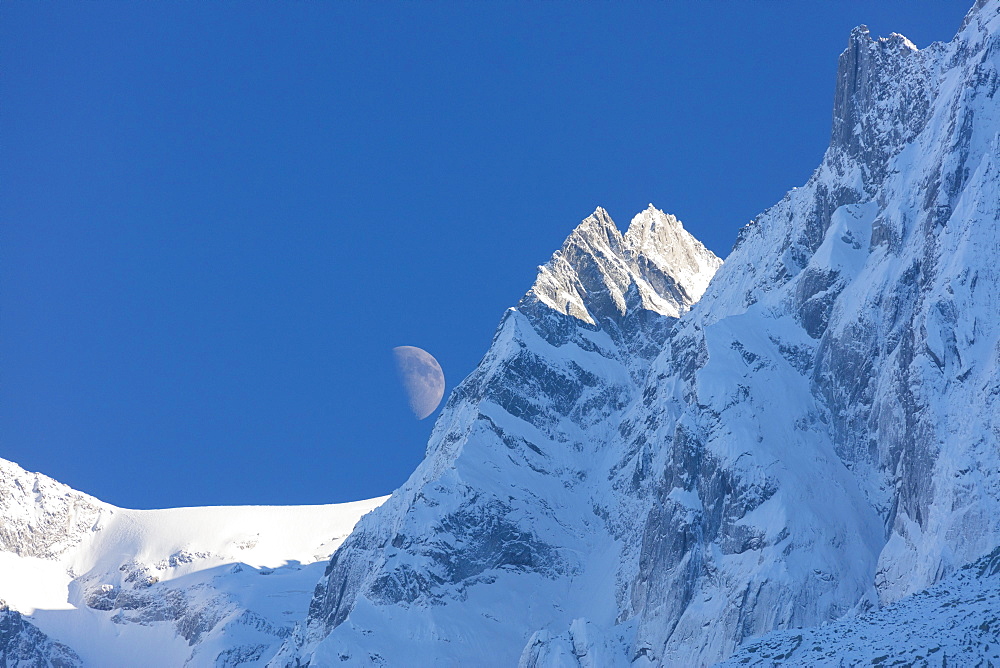 Blue sky and moon on the snowy ridges of the high peaks, Soglio, Bregaglia Valley, Canton of Graubunden, Switzerland, Europe