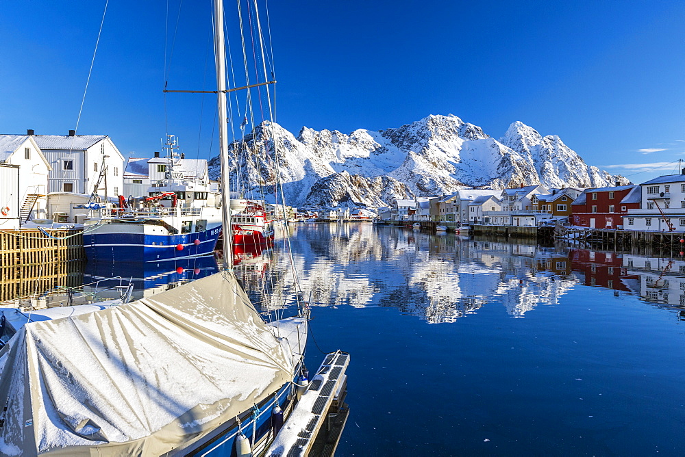 Boats docked in the calm waters of the port of Henningsvaer with the reflection of fishermen's houses and Norwegian Alps, Lofoten Islands, Arctic, Norway, Scandinavia, Europe