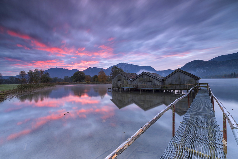 Purple sky at sunset and wooden huts are reflected in the clear water of Kochelsee, Schlehdorf, Bavaria, Germany, Europe