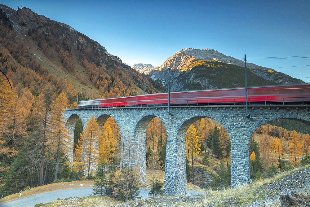 Red train on viaduct surrounded by colorful woods, Preda, Bergun, Albula Valley, Canton of Graubunden, Engadine, Switzerland, Europe