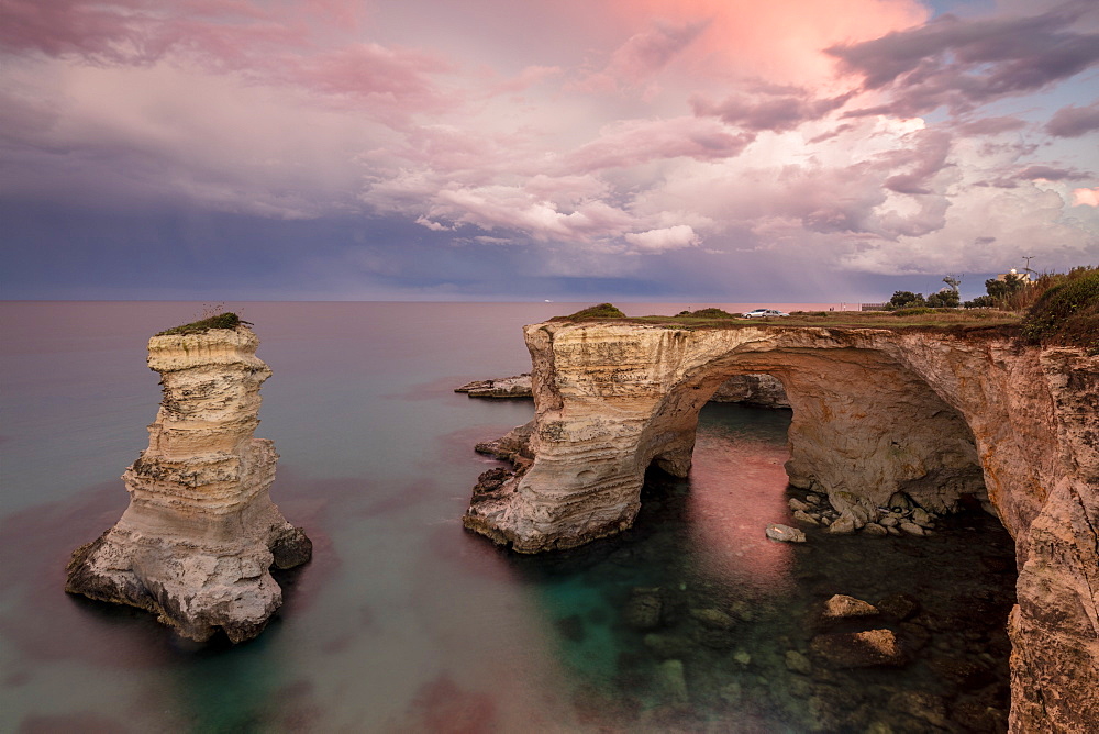 Pink sunset frames the cliffs known as Faraglioni di Sant'Andrea and the turquoise sea, province of Lecce, Apulia, Italy, Europe