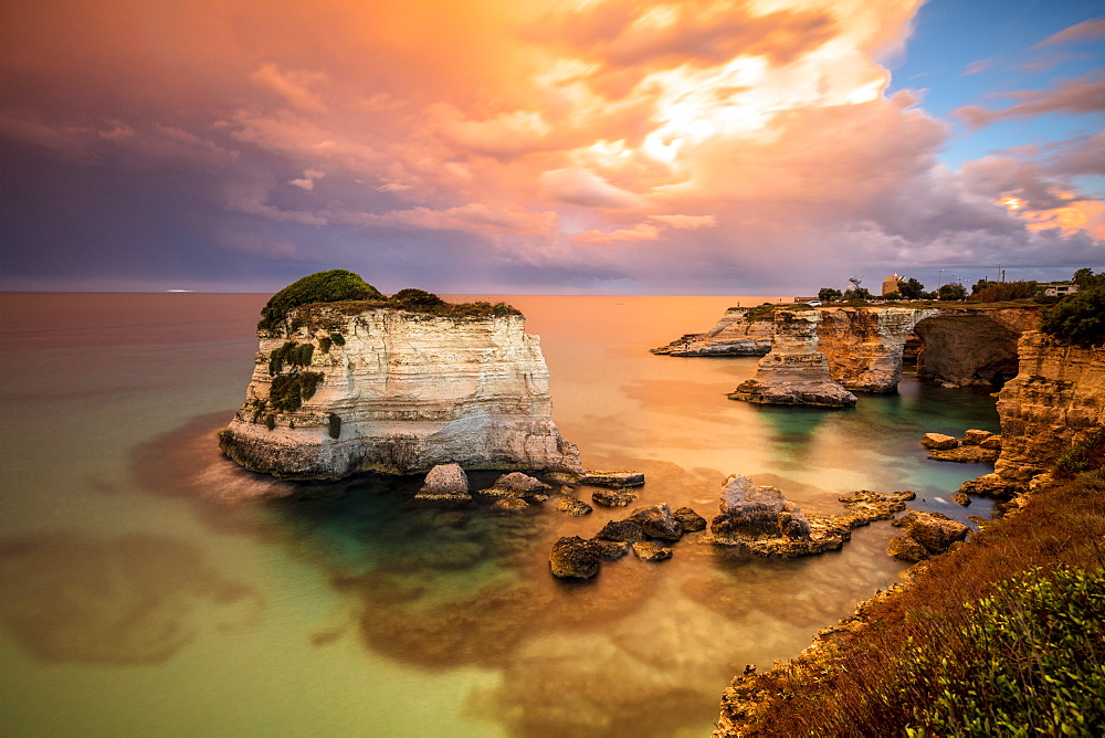 Sunset frames the high cliffs known as Faraglioni di Sant'Andrea and the turquoise sea, province of Lecce, Apulia, Italy, Europe