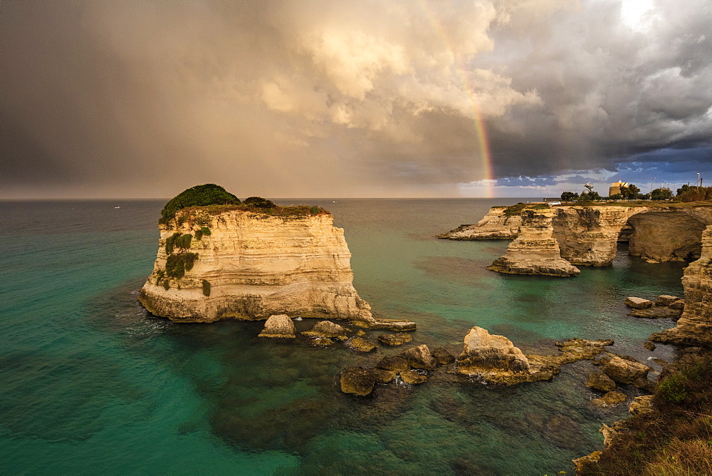 Rainbow frames rocky cliffs known as Faraglioni di Sant'andrea surrounded by turquoise sea, province of Lecce, Apulia, Italy, Europe