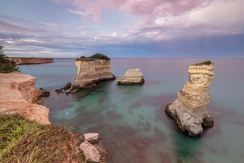 Pink sunset frames the cliffs known as Faraglioni di Sant'Andrea and the turquoise sea, province of Lecce, Apulia, Italy, Europe