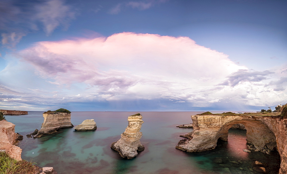 Pink sunset frames the cliffs known as Faraglioni di Sant'Andrea and the turquoise sea, province of Lecce, Apulia, Italy, Europe