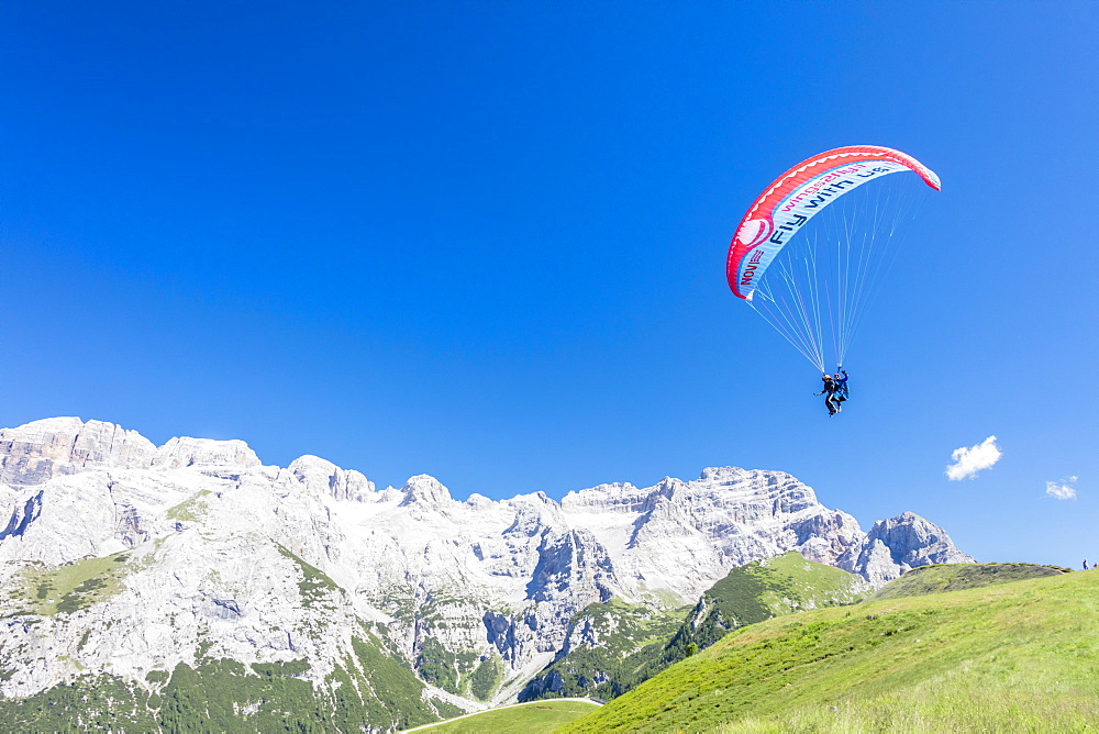 A paraglider among rocky peaks and green meadows Doss Del Sabion, Pinzolo, Brenta Dolomites, Trentino-Alto Adige, Italy, Europe