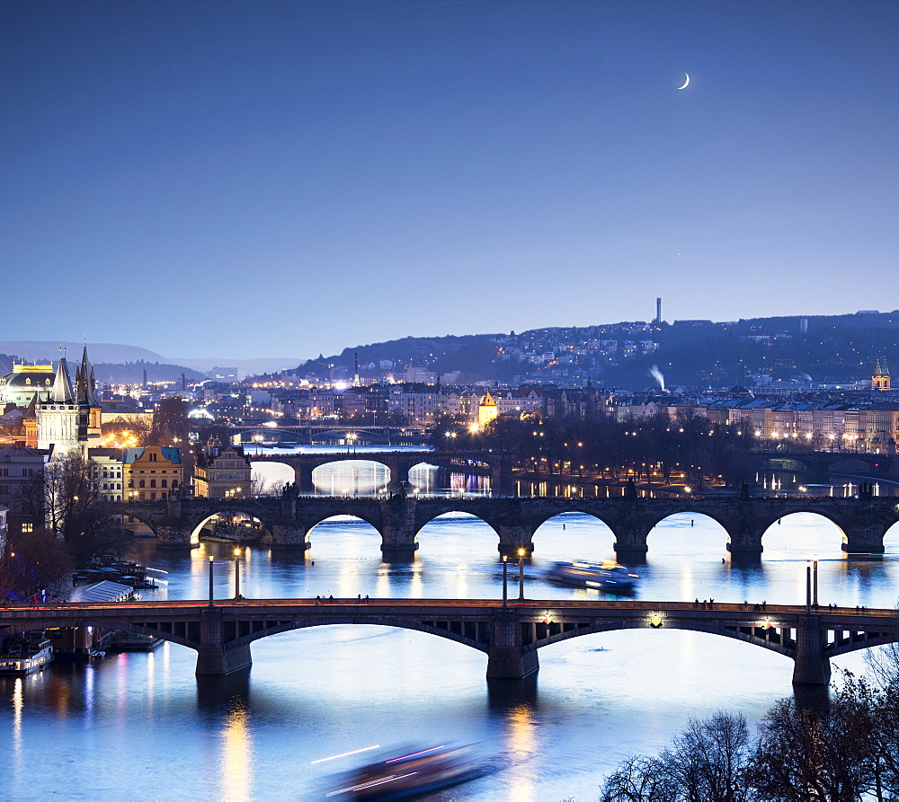 Dusk lights up the historical bridges and buildings reflected on Vltava River, Prague, Czech Republic, Europe