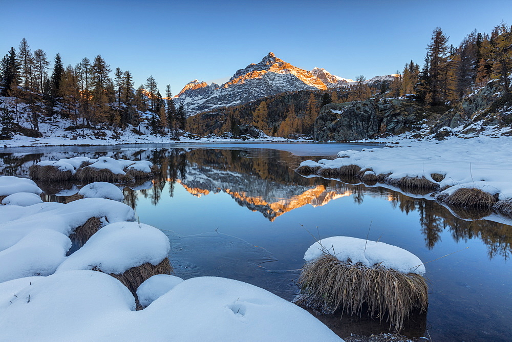 The rocky peak reflected in the frozen Lake Mufule at dawn, Malenco Valley, Province of Sondrio, Valtellina, Lombardy, Italy, Europe