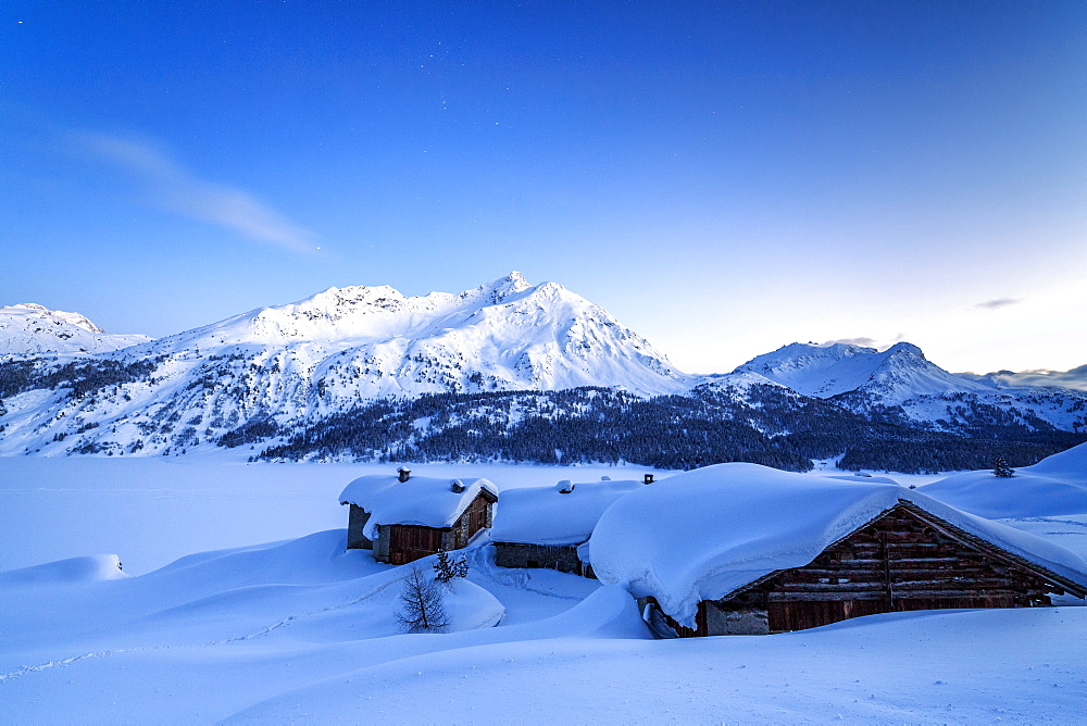 The blue hour leaving its place to the night over some scattered huts in Spluga by the Maloja Pass, Graubunden, Swiss Alps, Switzerland, Europe