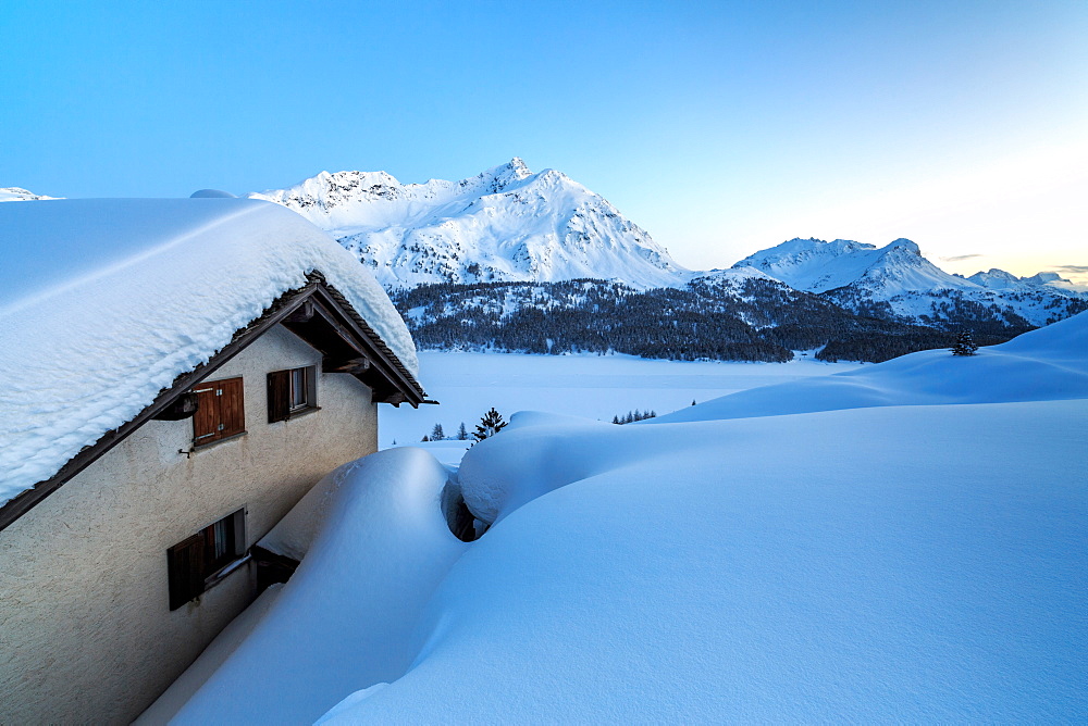 Enchanted atmosphere during the blue hour at Alp Spluga, with some scattered huts covered in snow, Graubunden, Swiss Alps, Switzerland, Europe