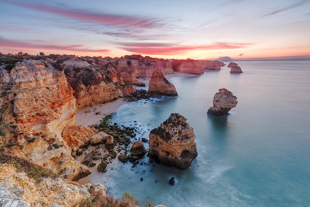 Sunrise on cliffs framed by turquoise water of the ocean, Praia da Marinha, Caramujeira, Lagoa Municipality, Algarve, Portugal, Europe