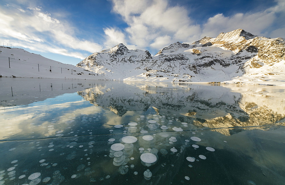 Ice bubbles frame the snowy peaks reflected in Lago Bianco, Bernina Pass, canton of Graubunden, Engadine, Switzerland, Europe