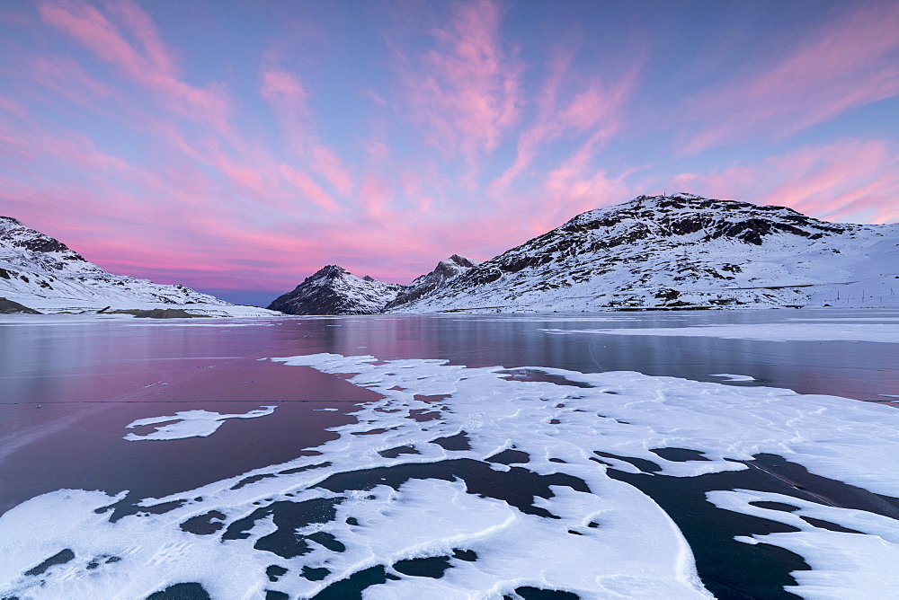 The frozen Lago Bianco framed by pink clouds at dawn, Bernina Pass, canton of Graubunden, Engadine, Switzerland, Europe