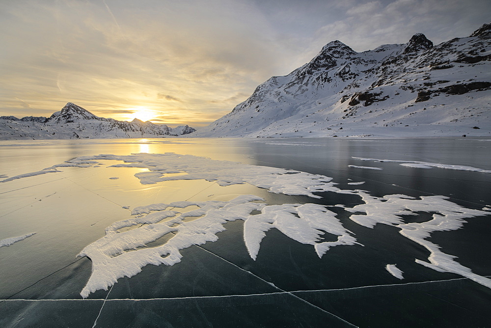 The frozen surface of Lago Bianco framed by snowy peaks at dawn, Bernina Pass, canton of Graubunden, Engadine, Switzerland, Europe