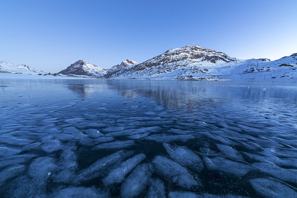 The frozen Lago Bianco framed the blue lights of dusk, Bernina Pass, canton of Graubunden, Engadine, Switzerland, Europe