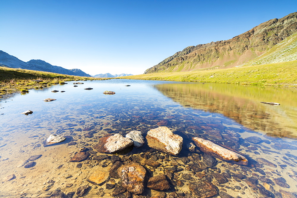 Sun shines on the rocky peaks reflected in the clear water of Lake Umbrail, Stelvio Pass, Valtellina, Lombardy, Italy, Europe