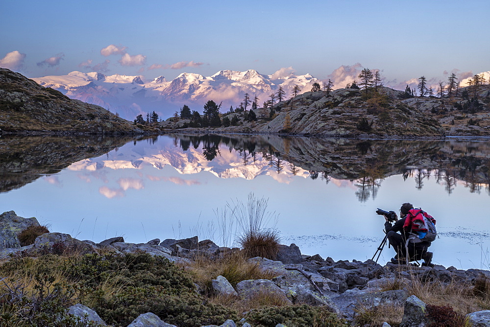 A photographer contemplating the sunset over the Monte Rosa from the Lake Bianco in the Mont Avic Natural Park, Aosta Valley, Italy, Europe