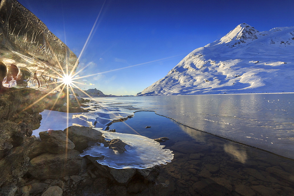 The sun shining through icicles formed on the shores of Lago Bianco at Bernina, completely frozen, Bernina Pass, Graubunden, Switzerland, Europe