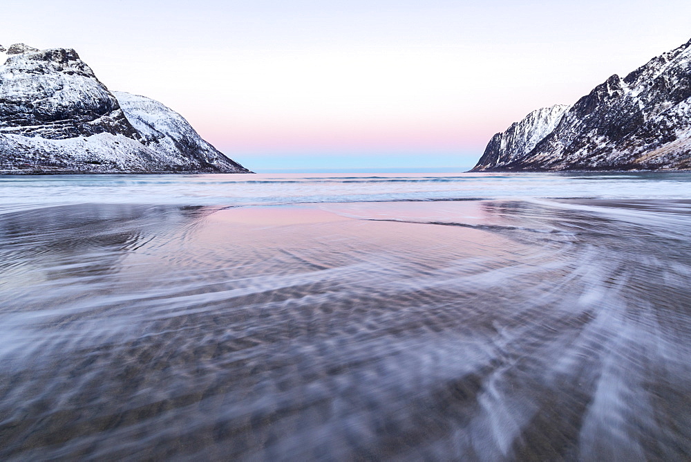 The pink light of sunrise over the waves of frozen sea surrounded by snowy peaks, Ersfjord, Senja, Troms, Norway, Scandinavia, Europe