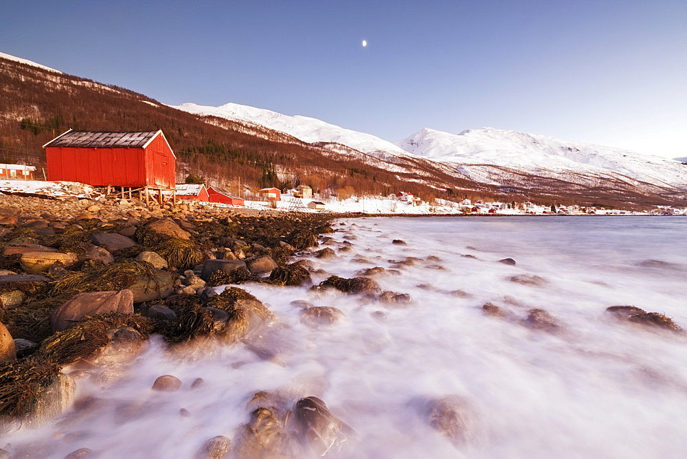 Waves of cold sea crashing on the rocks and typical wooden huts called Rorbu, Djupvik, Lyngen Alps, Troms, Norway, Scandinavia, Europe