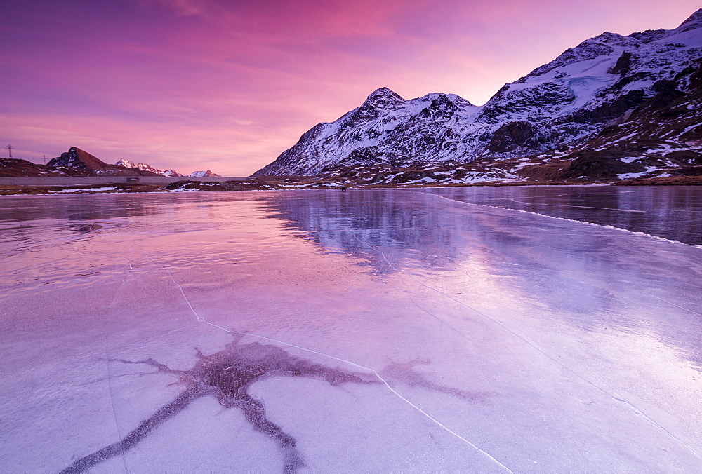 Pink sky at sunset on the frozen Lej Nair framed by snowy peaks, Bernina Pass, Canton of Graubunden, Engadine, Switzerland, Europe