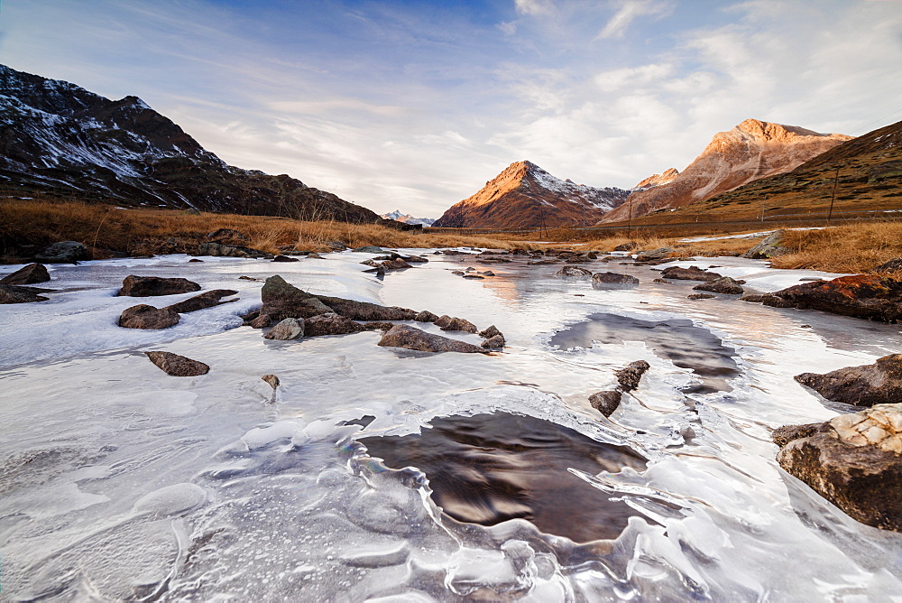 Sunset frames the alpine creek covered with ice at Bernina Pass, Canton of Graubunden, Engadine, Switzerland, Europe