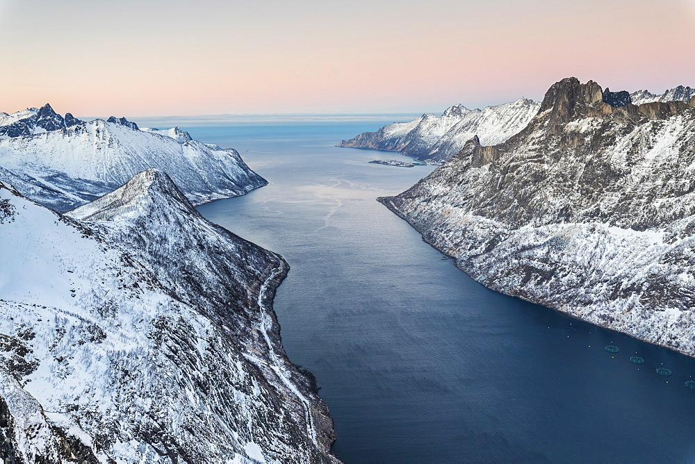 Top view of the snowy peaks surrounding Fjordgard framed by the frozen sea at sunset, Ornfjorden, Senja, Troms, Norway, Scandinavia, Europe