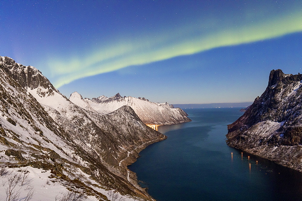 Northern Lights (aurora borealis) on the snowy peaks and the village of Fjordgard framed by the frozen sea, Ornfjorden, Senja, Troms, Norway, Scandinavia, Europe