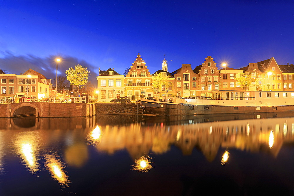 Dusk lights on typical houses and bridge reflected in a canal of the River Spaarne, Haarlem, North Holland, The Netherlands, Europe