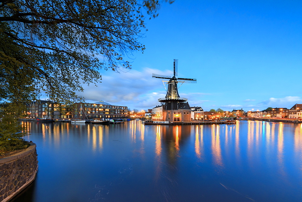 Dusk lights on the Windmill De Adriaan reflected in the River Spaarne, Haarlem, North Holland, The Netherlands, Europe