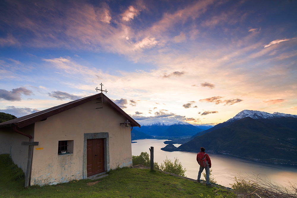 Hiker at the church of San Domenico admires Lake Como framed by pink sky at dawn, Cremia, Lombardy, Italian Lakes, Italy, Europe