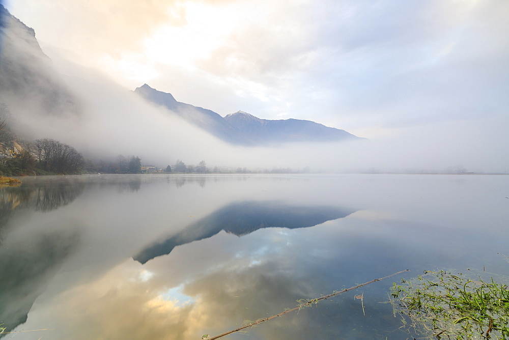 Mountains reflected in water at dawn shrouded by mist, Pozzo di Riva Novate, Mezzola, Chiavenna Valley, Lombardy, Italy, Europe