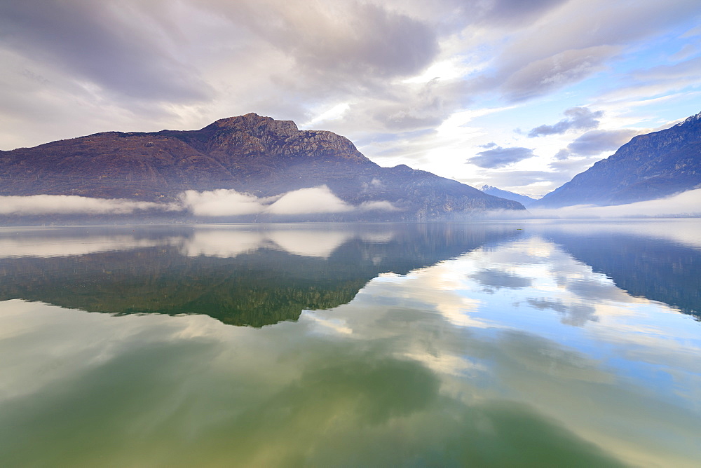 Mountains reflected in Lake Mezzola at dawn shrouded by mist, Verceia, Chiavenna Valley, Lombardy, Italy, Europe