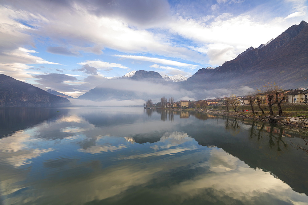 Mountains and village are reflected in Lake Mezzola at dawn shrouded by mist, Verceia, Chiavenna Valley, Lombardy, Italy, Europe