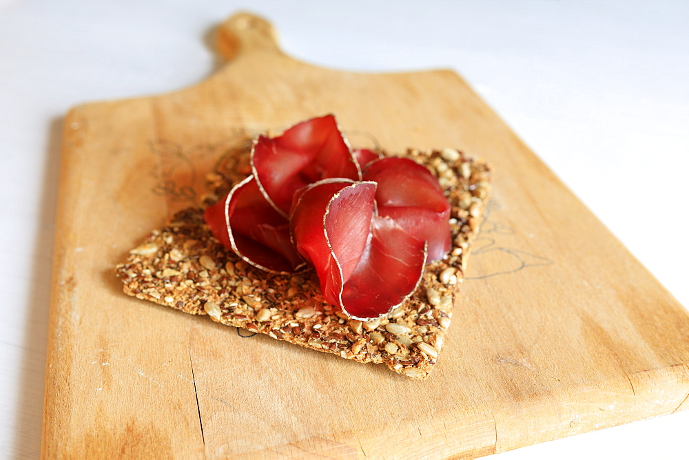 Slices of Bresaola a typical raw beef cured by salting and air-drying, on wooden cutting board, Valtellina, Lombardy, Italy, Europe