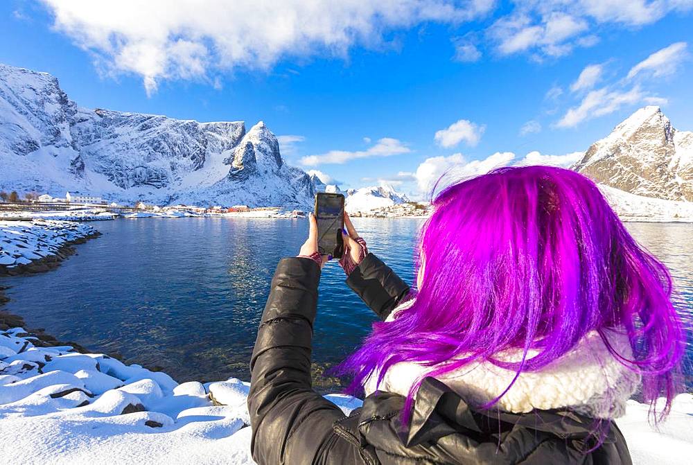 Woman with fuchsia hair taking photo with smartphone, Reine Bay, Lofoten Islands, Nordland, Norway, Europe