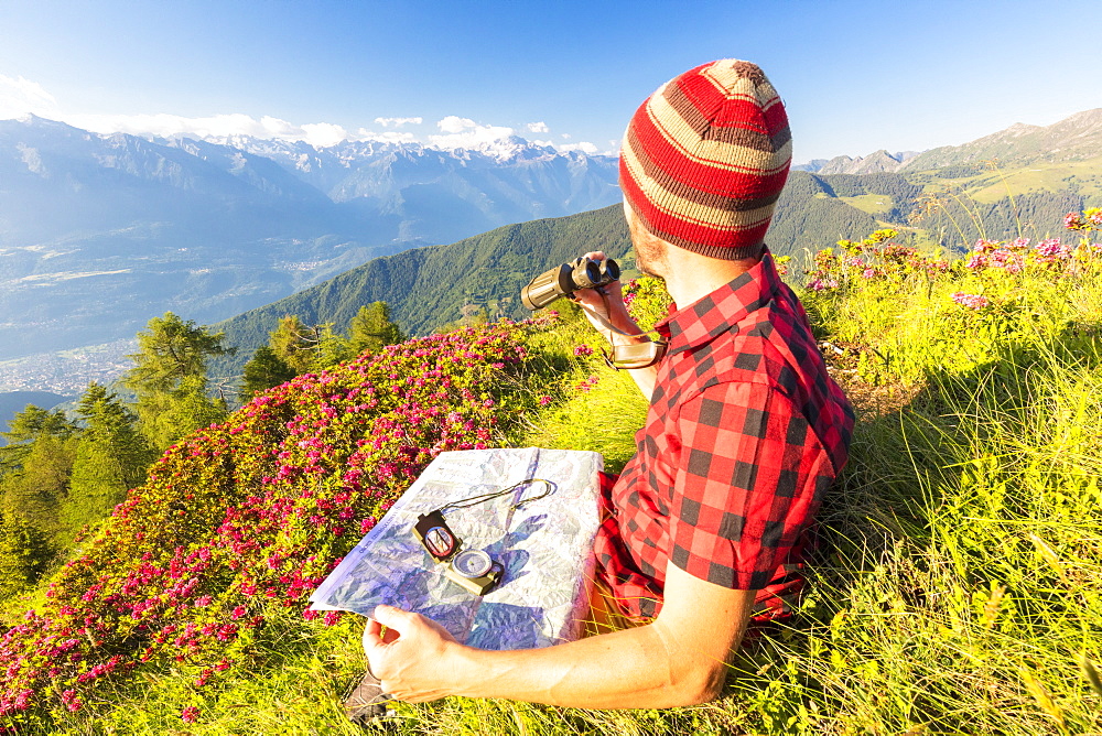 Hiker with map and binoculars looks towards Rhaetian Alps and Monte Disgrazia from Pizzo Berro, Bitto Valley, Lombardy, Italy, Europe