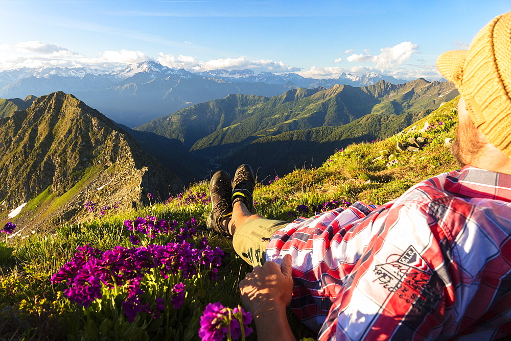 Man lying down on top of Monte Azzarini looks towards Monte Disgrazia and Monte Pedena, Albaredo Valley, Orobie Alps, Lombardy, Italy, Europe