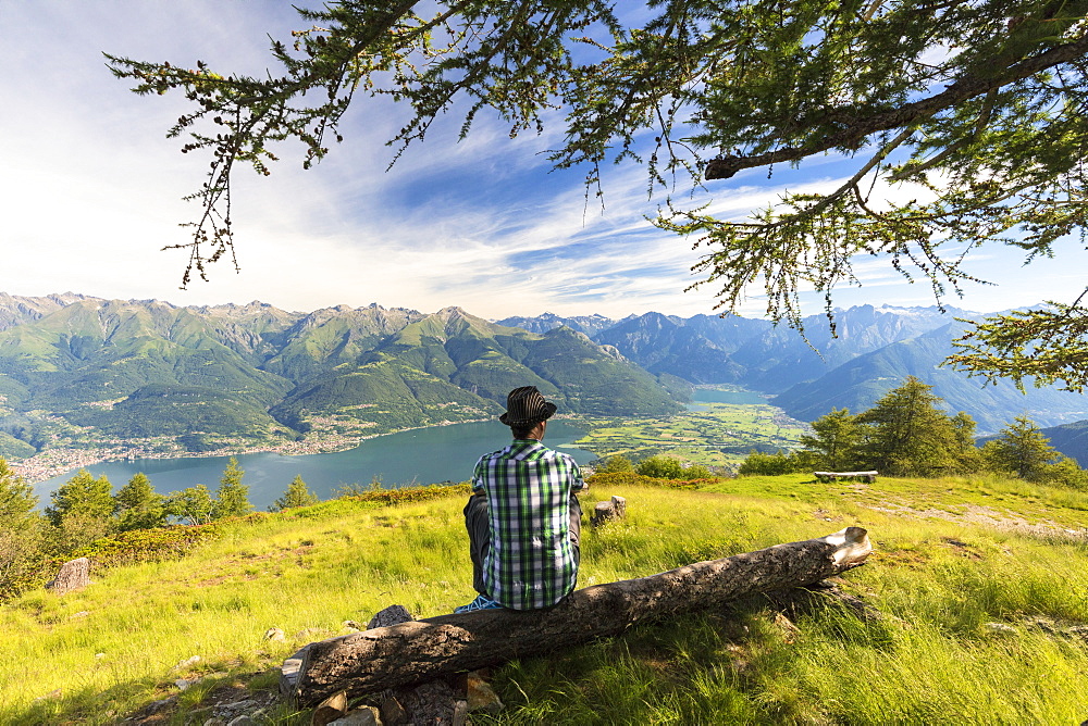 Man sitting on tree trunk looks towards Lake Como and Alto Lario, Monte Legnoncino, Lecco province, Lombardy, Italy, Europe