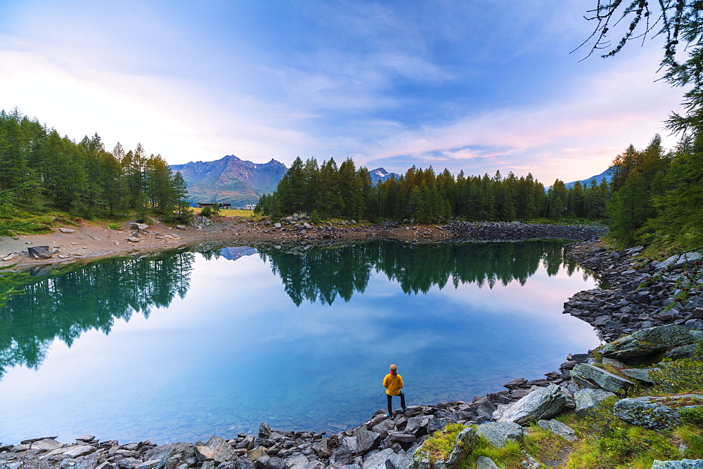 Hiker admires sunrise on lakeshore, Lago Azzurro, Spluga Valley, Sondrio province, Valtellina, Lombardy, Italy, Europe